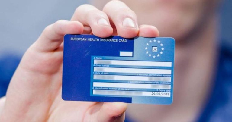 Un pensionar ținând în mână Cardul European de Asigurări de Sănătate cu un spital public pe fundal