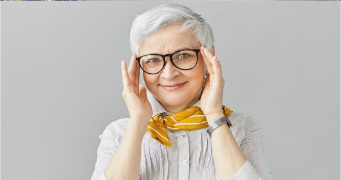 O pensionară probând fericită o pereche nouă de ochelari de vedere într-un cabinet de optică medicală