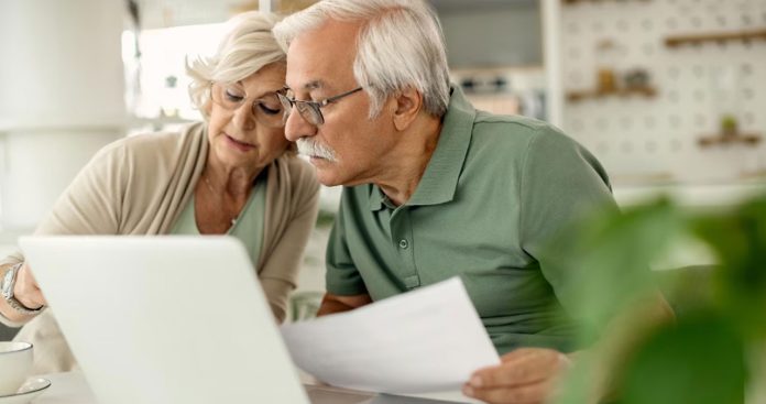 Pensionar semnând un contract de credit bancar alături de un ofițer, ilustrând creditele pentru pensionari și condiția asigurării de viață