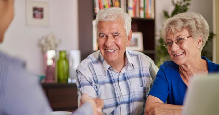 Un pensionar zâmbind în timp ce semnează un contract de credit bancar de nevoi personale la biroul unui ofițer de cont