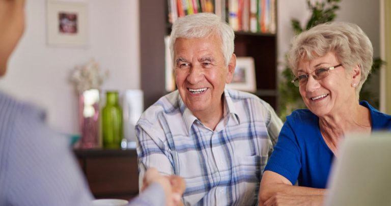 Un pensionar zâmbind în timp ce semnează un contract de credit bancar de nevoi personale la biroul unui ofițer de cont